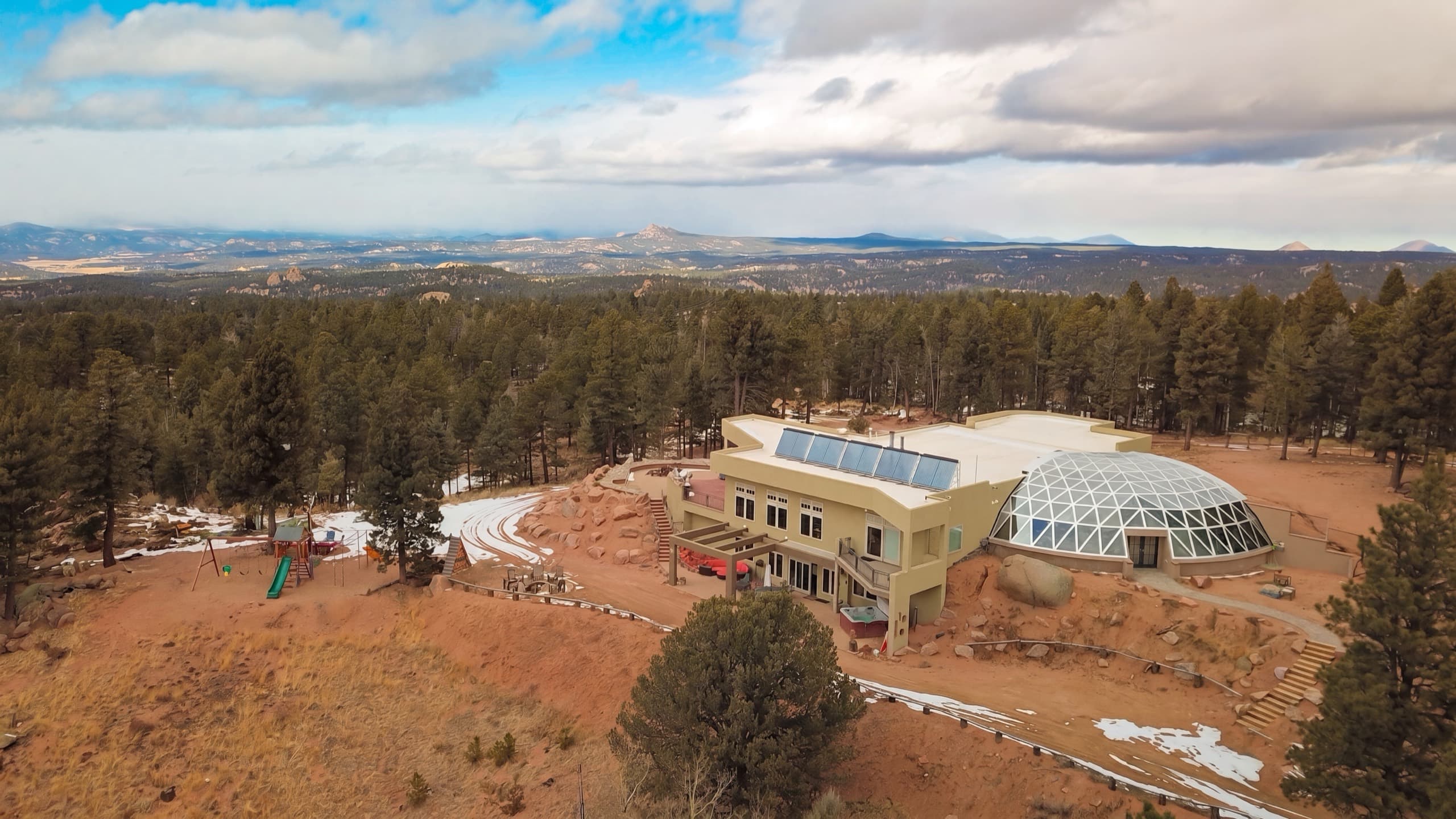 Kutsu Point from the air: the lodge and glass geodesic dome alone on a forty-acre ridge, mountains beyond