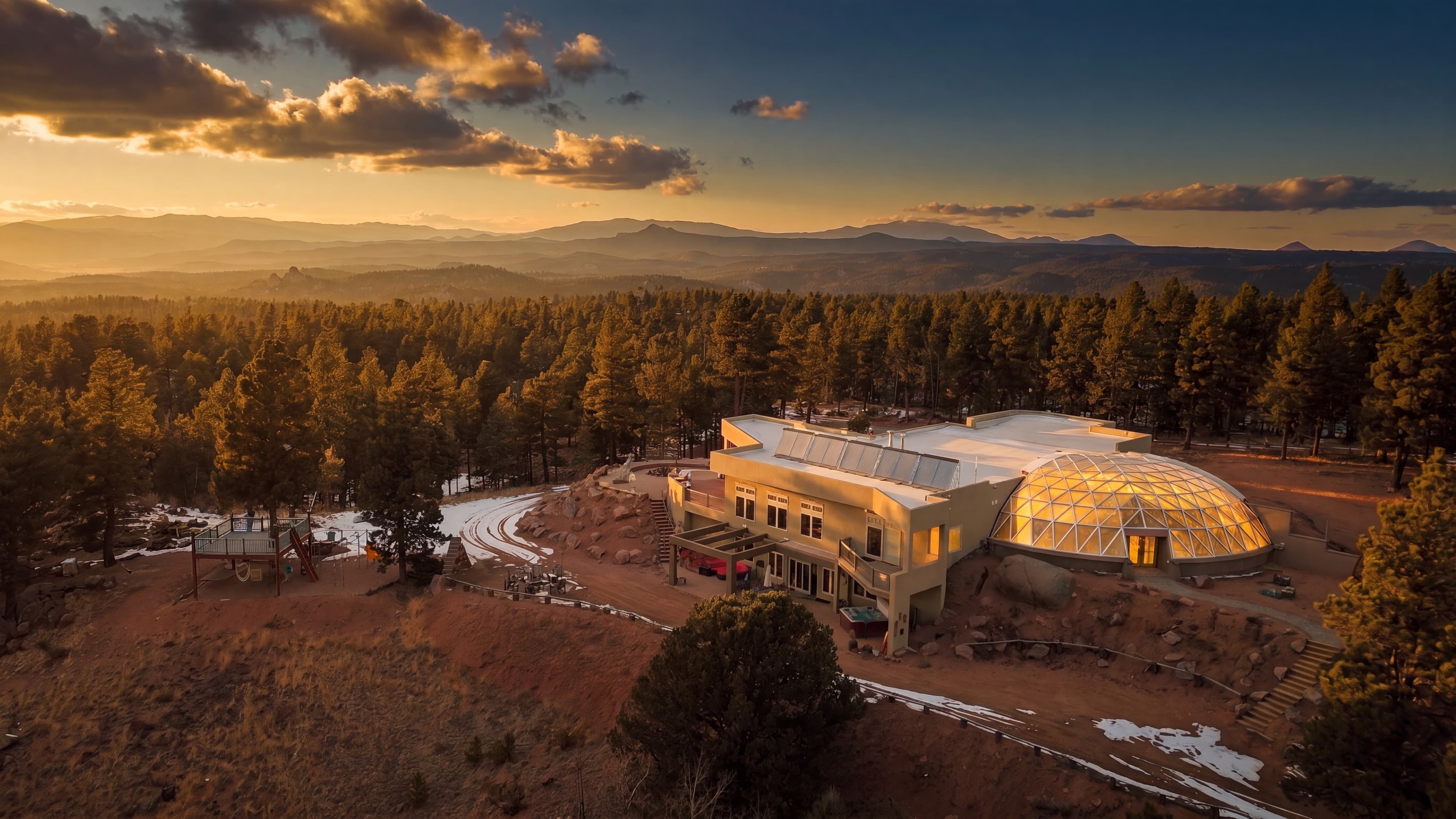 Kutsu Point at last light: the lodge and glowing glass geodesic dome alone on a forty-acre ridge, mountains beyond